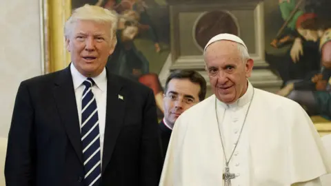 Reuters US President Donald Trump, wearing a suit, and Pope Francis, dressed in papal guard, stand beside each other while being photographed in the Vatican