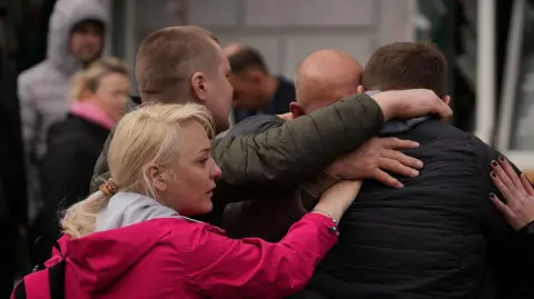 Getty Images People embrace and cry at the site of Russian ballistic strike on April 13, 2025 in Sumy, Ukraine