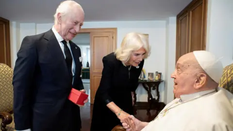 Reuters King Charles III pictured standing next to Queen Camilla who is shaking Pope Francis's hand while the Pope is seated