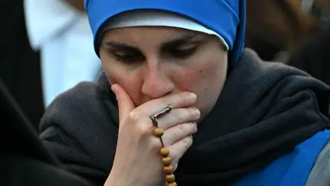 Getty Images A woman holds her face, with prayer beads wrapped around her fingers while she mourns for Pope Francis in St Peter's Square after the news of his death on 21 April, 2025.